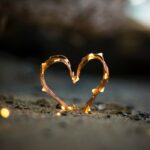 close-up photography of heart shaped fairy lite on brown sand